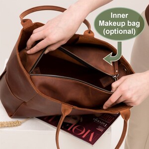 May include: A brown leather tote bag with a zippered top opening. The bag has two handles and is open to reveal a brown fabric lining. The text "Inner Makeup bag (optional)" is written on a green label.