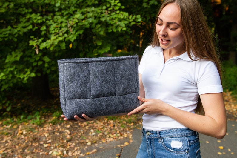 May include: A grey felt tote bag with a quilted design. The bag is being held by a person in front of a green background.