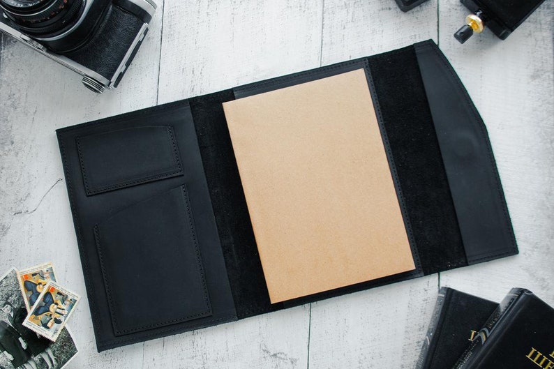 May include: A black leather portfolio with a brown paper insert and two pockets on the front. The portfolio is open and the paper insert is visible.