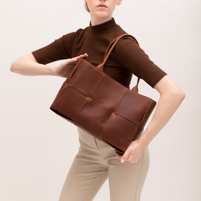 May include: A brown leather tote bag with a woven design. The bag has two top handles and a zipper closure.