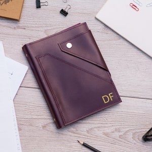 May include: Burgundy leather journal with a gold snap closure and a pocket on the front. The journal has the initials "DF" embossed in gold on the front cover.