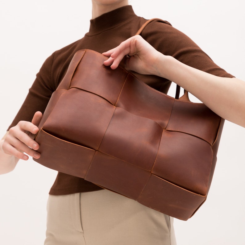 May include: A brown leather tote bag with a woven design. The bag has two top handles and a spacious interior.