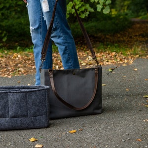 May include: A grey felt bag organiser with multiple compartments sits next to a grey canvas tote bag with brown leather straps.