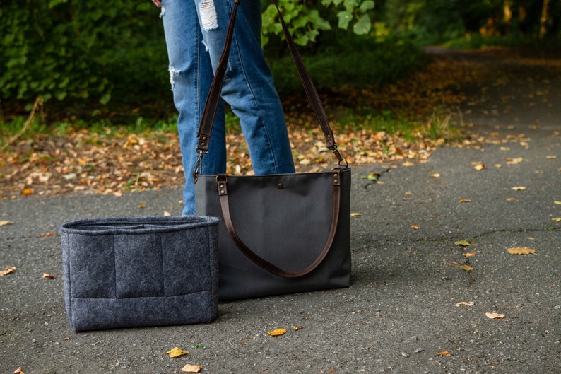 May include: A grey felt bag organiser with multiple compartments sits next to a grey canvas tote bag with brown leather straps.