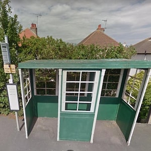 Peut inclure: Un abribus vert avec un toit blanc et des fenêtres à encadrement blanc. L'abribus a un panneau avec le texte "10.20 am & 1.10 pm Mon - Fri".