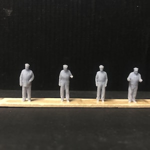 Puede incluir: Siete figuritas de plástico gris de personas con sombreros de pie en fila sobre una superficie de madera.