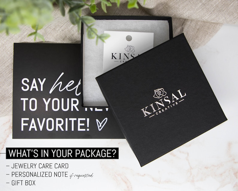 May include: A black gift box with a white rose and the text "KINSAL - CREATIVE" on the lid. The box is sitting on a white marble surface. The text "SAY hello TO YOUR FAVORITE!" is on a black card in the background.