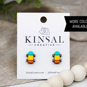 May include: A pair of colorful wooden skateboard earrings. The earrings are painted in shades of turquoise, yellow, and orange. The earrings are displayed on a white card with the text "Kinsal Creative" and "More Colors Available!"