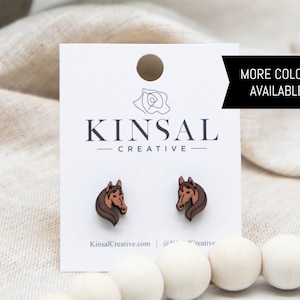May include: A pair of brown wooden horse head stud earrings on a white card with the text "Kinsal Creative" and "More Colors Available!"