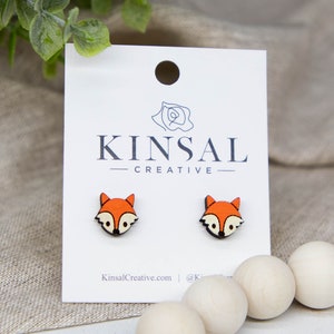 May include: A pair of wooden fox stud earrings on a white card with the text "Kinsal Creative" and the website address "KinsalCreative.com".