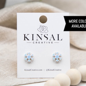 May include: A pair of iridescent snowflake stud earrings on a white card with the text "Kinsal Creative" and "More Colors Available!"