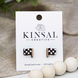 Puede incluir: Un par de pendientes de madera con un diseño de bandera a cuadros. Los pendientes son negros y blancos con un acento dorado. Los pendientes se muestran en una tarjeta blanca con el texto "Kinsal Creative" impreso en ella.