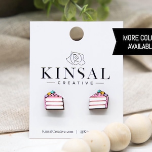 May include: Wooden stud earrings featuring a slice of cake design with pink frosting, white layers, and colorful sprinkles. The earrings are displayed on a white card with the text "KINSAL CREATIVE" and "MORE COLORS AVAILABLE!"