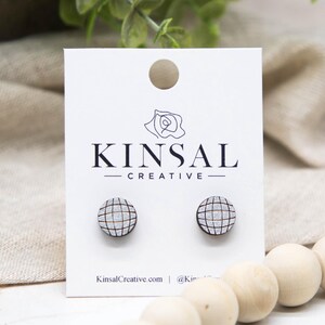 May include: Wooden stud earrings with a grid pattern, displayed on a white card with the "KINSAL CREATIVE" logo. The earrings are round with a gray and black design. The card also includes the website KinsalCreative.com.