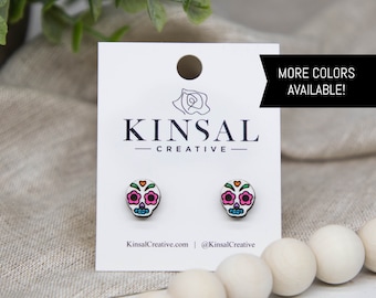 May include: A pair of white wooden earrings featuring a colourful sugar skull design. The earrings are displayed on a white card with the text "Kinsal Creative" and "More Colors Available!"