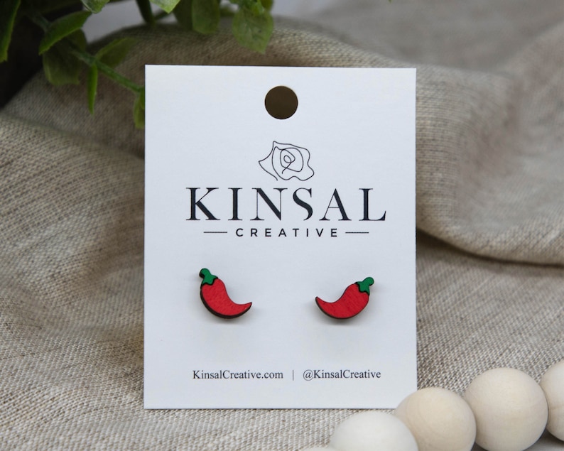 May include: A pair of red chili pepper earrings on a white card with the text "Kinsal Creative".