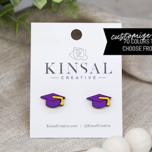 May include: Purple and yellow graduation cap earrings on a white card with the text "Kinsal Creative" and "customize me 70 colors to choose from!"  KinsalCreative.com and @KinsalCreative are also printed on the card.