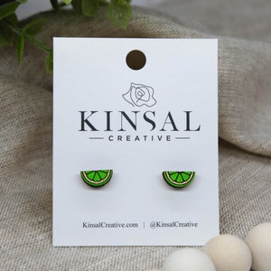 May include: A pair of lime wedge earrings on a white card with the text "Kinsal Creative" printed on it. The earrings are made of wood and painted green and yellow.
