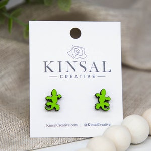 May include: A pair of green lizard stud earrings on a white card with the text "Kinsal Creative" printed on it.