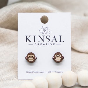 May include: A pair of wooden monkey stud earrings on a white card with the text "Kinsal Creative".