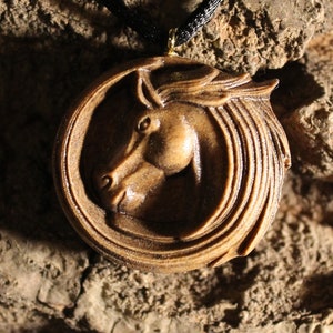 May include: A wooden pendant necklace featuring a carved horse head design. The pendant is round and has a dark brown color. The horse's mane is flowing and detailed.