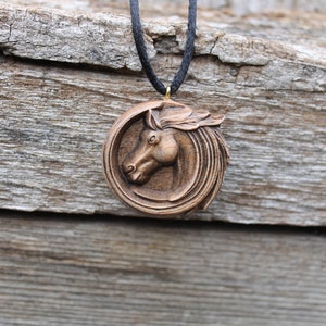May include: A wooden horse head pendant necklace with a brown cord. The horse head is carved in detail and is surrounded by a circular design.