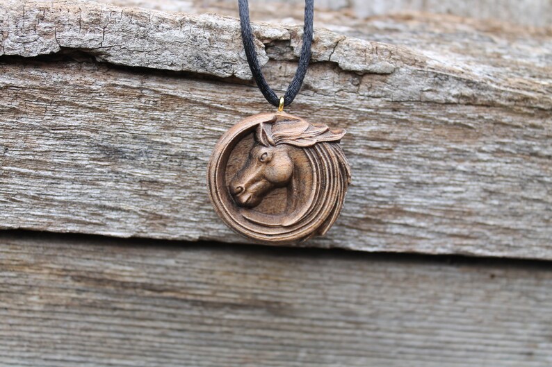 May include: A wooden horse head pendant necklace with a brown cord. The horse head is carved in detail and is surrounded by a circular design.