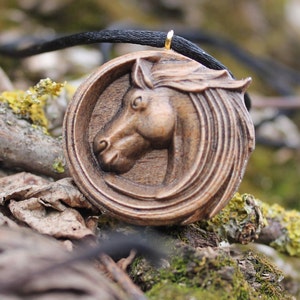 May include: A wooden horse head pendant necklace with a black cord. The pendant is carved in detail and has a gold-colored bail.