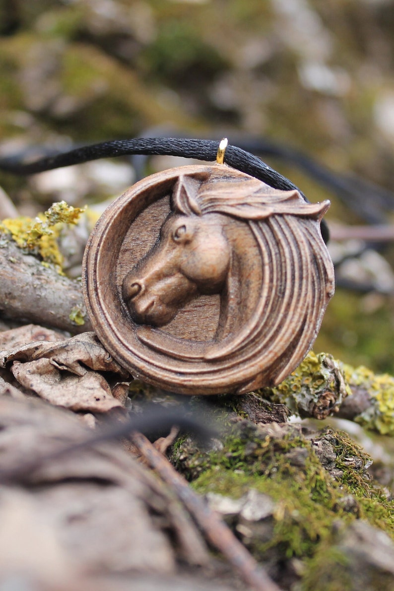May include: A wooden horse head pendant necklace with a black cord. The pendant is carved in detail and has a gold-colored bail.