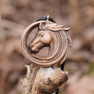 May include: A wooden horse head pendant with a dark brown finish. The pendant is carved in detail and has a gold-colored bail.