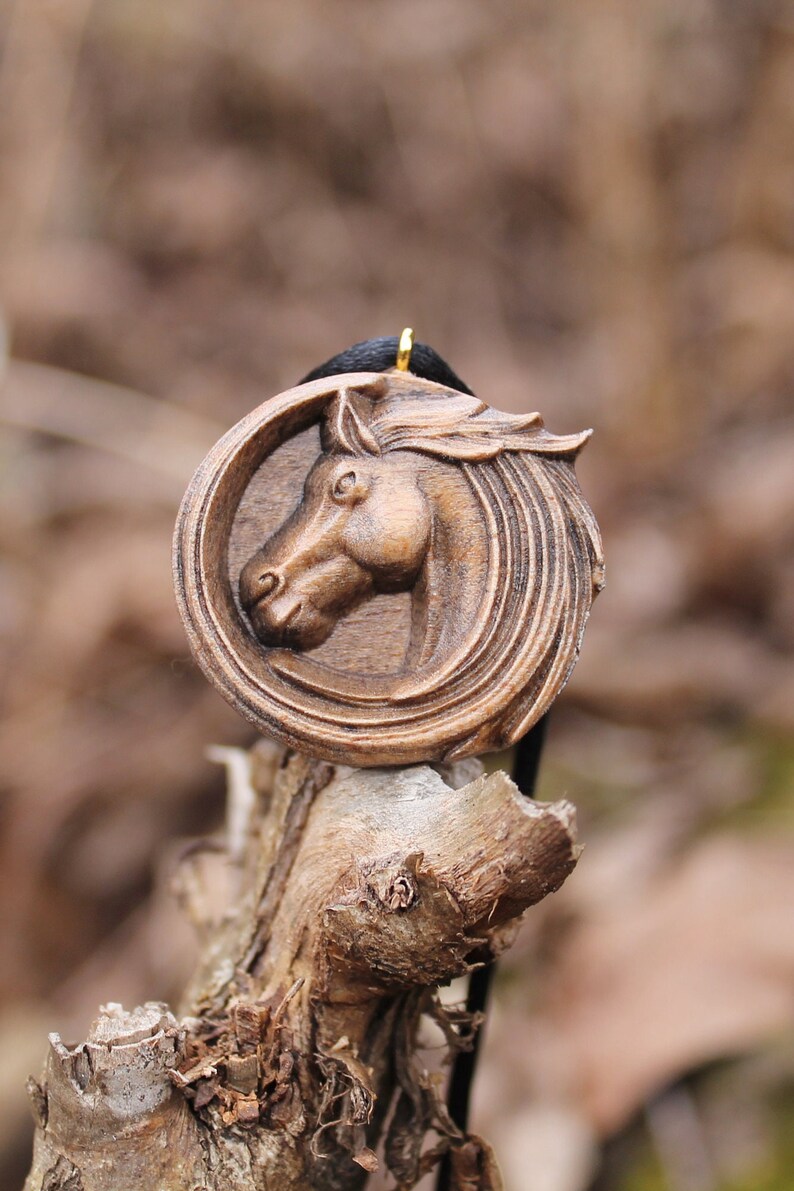 May include: A wooden horse head pendant with a dark brown finish. The pendant is carved in detail and has a gold-colored bail.