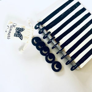 May include: A disc-bound planner featuring a black and white striped cover, accompanied by a set of loose black plastic binding discs and a small cream-colored drawstring pouch printed with a black butterfly graphic and the text Planners.