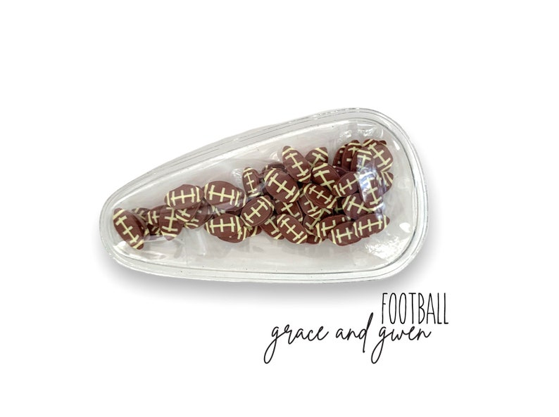 May include: A clear plastic football-shaped container filled with small brown and white football-shaped charms. The text "FOOTBALL grace and given" is written below the container.