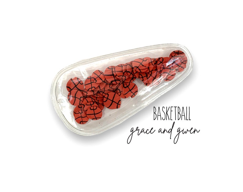 May include: Clear plastic hair clip filled with red and black basketball-themed confetti. The text "BASKETBALL grace and guen" is printed below the clip.