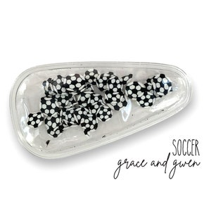 May include: A clear plastic hair clip with a black and white soccer ball design. The text "SOCCER grace and gwen" is printed below the clip.