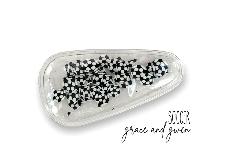 May include: A clear plastic hair clip with a black and white soccer ball design. The text "SOCCER grace and gwen" is printed below the clip.