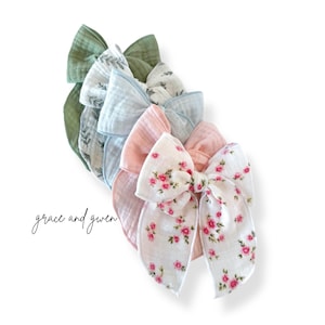 May include: A set of five fabric hair bows in various colors and patterns. The bows are made of soft, gauzy fabric and feature floral prints and a simple leaf design. The bows are arranged in a stack, with the largest bow on the bottom and the smallest bow on top. The text "grace and given" is visible in the lower left corner of the image.