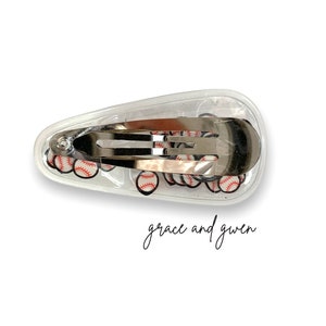 May include: A clear plastic hair clip with a silver metal clasp. The clip is filled with small baseball-themed images.