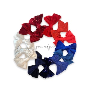 May include: A set of eight hair bows in red, white, and blue colors. The bows are made of velvet and have a variety of textures, including sequins and polka dots. The bows are arranged in a circle, with the text "grace and given" in the center.