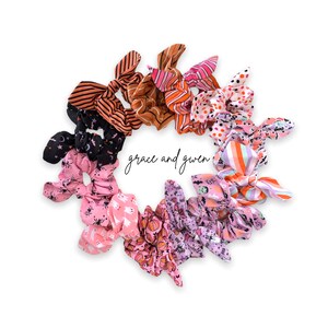 May include: A set of ten Halloween-themed hair scrunchies in various colors and patterns, including pink, orange, black, and white. The scrunchies feature spooky designs like ghosts, bats, and pumpkins. The text "grace and given" is visible in the center of the image.