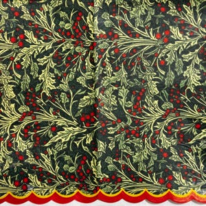 Op de afbeelding: Een vel stof of papier met een dicht botanisch patroon van donkergroene hulstbladeren en felrode bessen op een zwarte achtergrond, afgewerkt met een decoratieve geschulpte rand die langs de onderkant geel en rood is afgezet.