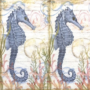 Op de afbeelding: Een decoratief papieren servet met een herhalend patroon van twee donkerblauwe zeepaardjes tussen groen zeewier, roze koraal en ronde zanddollars. De achtergrond heeft een lichtbeige houtnerftextuur met vage blauwe wervelingen.