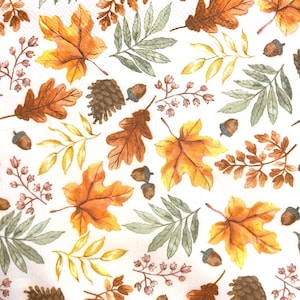 May include: A white paper napkin featuring a repeating pattern of autumn elements including orange and yellow maple leaves, brown oak leaves, green fern-like foliage, small brown acorns, and dark brown pinecones scattered across the surface.