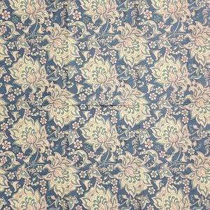 May include: A fabric with a repeating floral pattern. The design features large, stylized flowers in cream, light green, and pink, set against a deep blue background. Smaller white flowers and vines fill the spaces between the larger blooms.