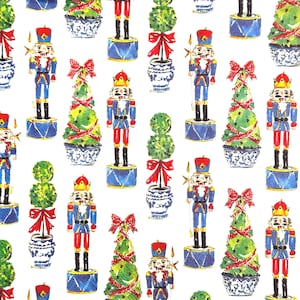 May include: A repeating pattern on a white background featuring watercolour illustrations of nutcracker figures in blue and red uniforms, green topiary trees in blue and white patterned pots, and green cone-shaped trees with red ribbons.