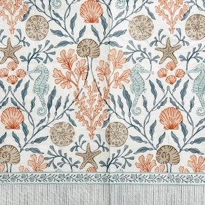May include: White paper napkin with a repeating pattern of sea creatures and plants. The design includes starfish, seashells, seahorses, and coral in shades of peach, blue, and brown. A striped border frames the bottom.