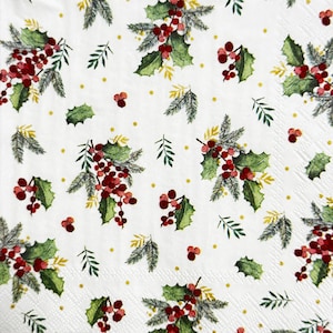 May include: White paper napkin with a repeating pattern of red berries, green holly leaves, and sprigs of pine needles. Small yellow dots are scattered throughout the design. The napkin has a textured surface.