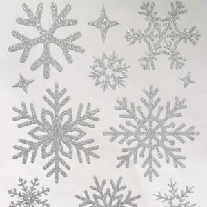 May include: A collection of silver glitter snowflake and star stickers in various sizes. The stickers have a sparkly texture and are arranged on a white background. Ideal for holiday crafts and decorations.