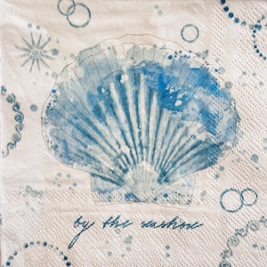 May include: A white paper napkin with a blue watercolor seashell design. The seashell is the focal point, with radiating lines and blue watercolor accents. The words "by the seashore" are written in cursive.