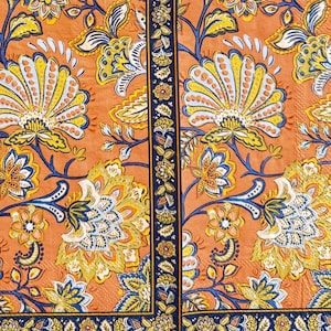 May include: An orange floral pattern with yellow, blue, and white accents. The design features large stylized flowers and leaves, with a dark blue border and central stripe. The overall aesthetic is reminiscent of vintage textiles.
